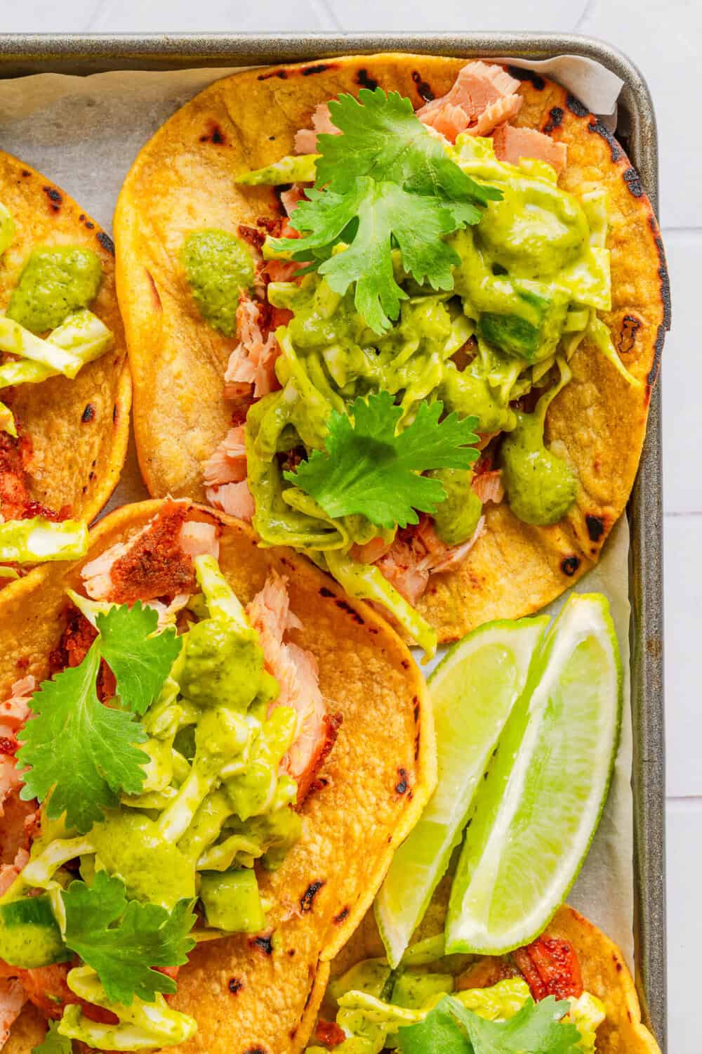 Tray of roasted salmon tacos with cilantro lime salt with limes on the tray with it.
