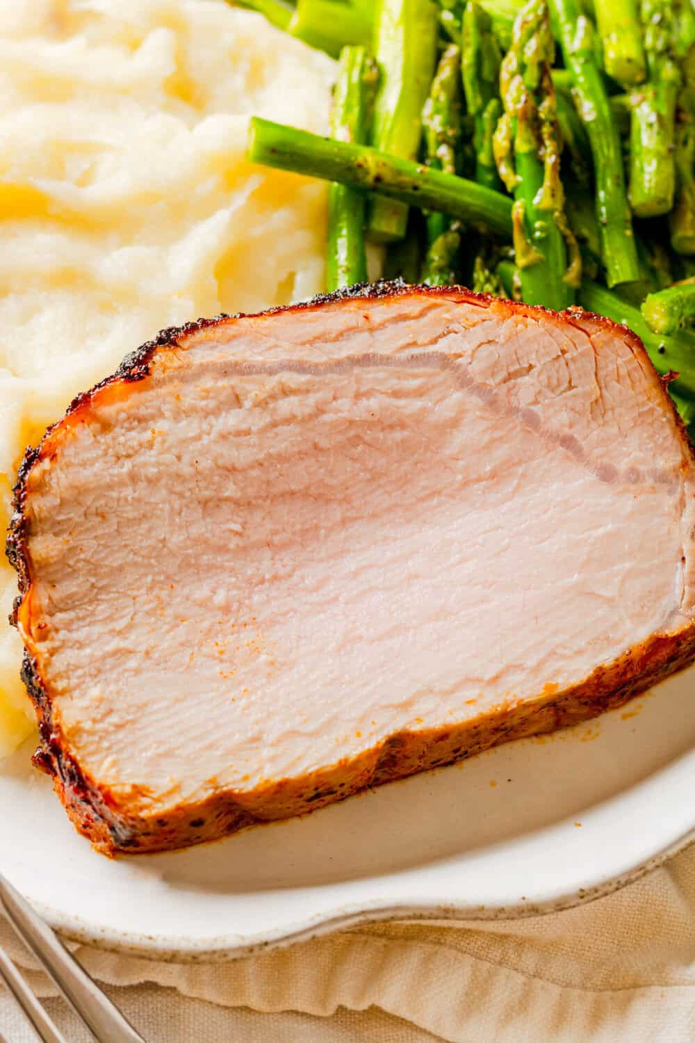 Slice of pork loin in the air fryer on a plate with mashed potatoes and asparagus. 