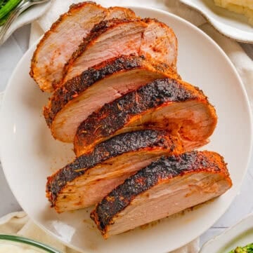 Air fryer pork loin sliced on a plate with healthy sides around it in bowls.