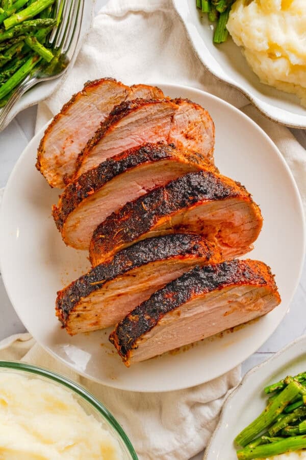 Air fryer pork loin sliced on a plate with healthy sides around it in bowls.