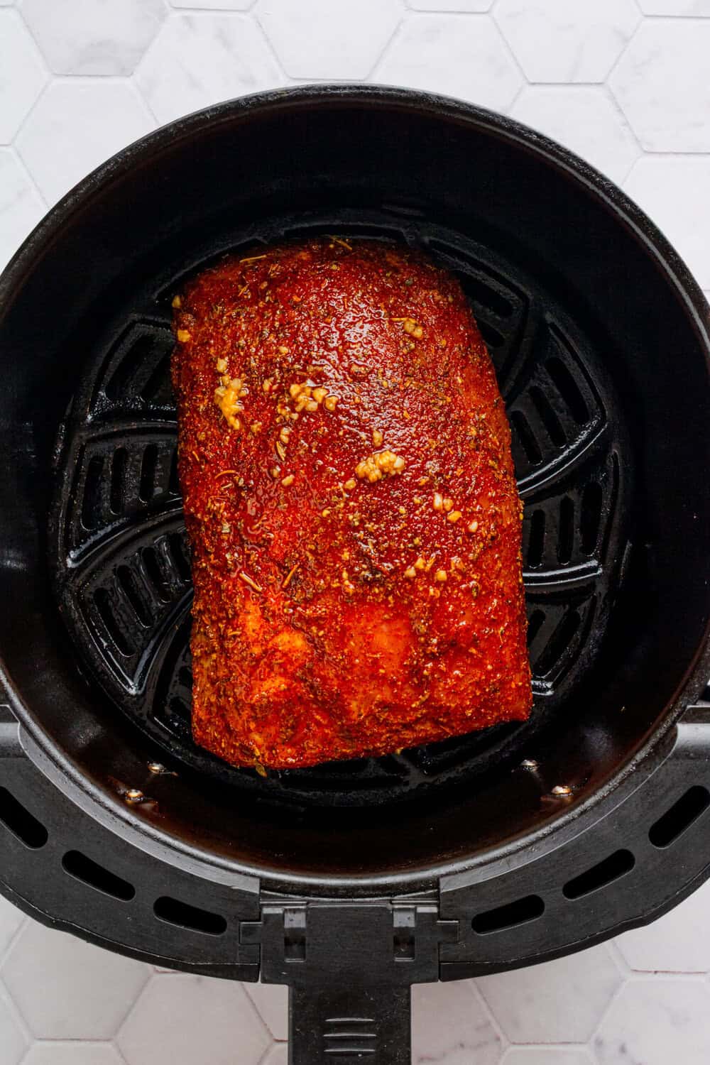 Seasoned pork loin uncooked in a a black air fryer basket. 