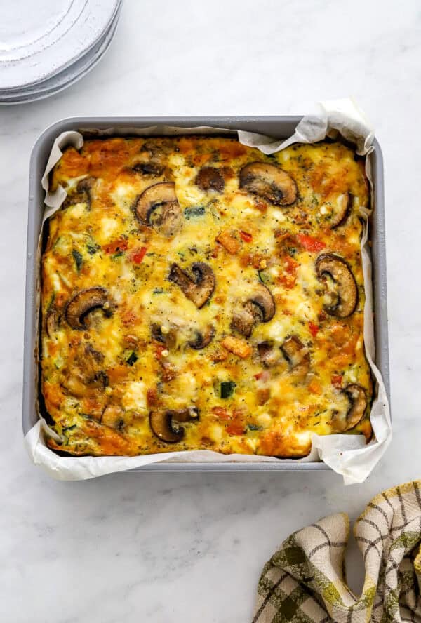 Square pan filled with veggie frittata baked until golden with a plaid towel in front of it.