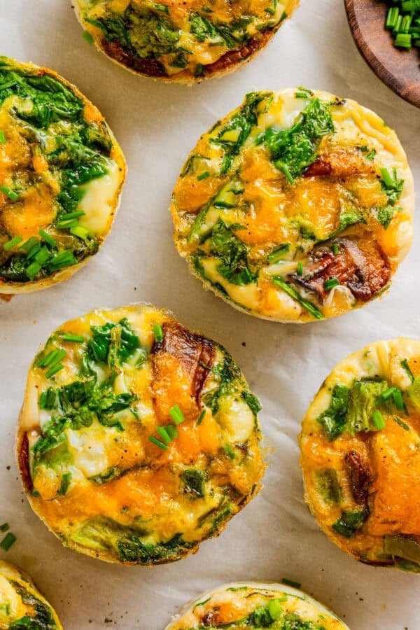 Several egg muffins with veggies and cheese with more around them.
