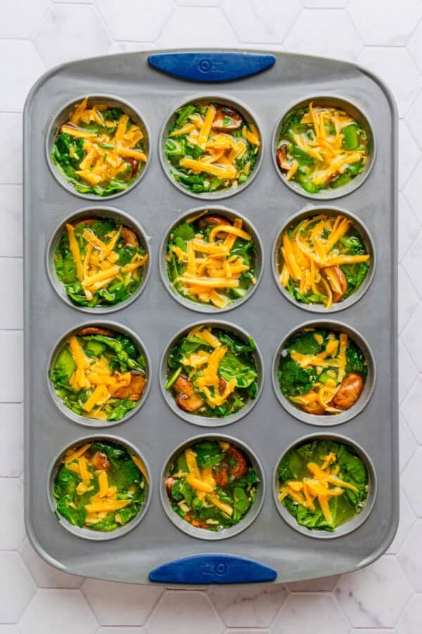 Metal muffin pan with uncooked egg white muffin mixture with veggies in it.
