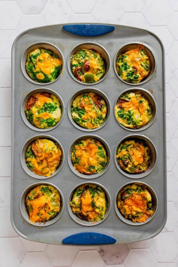 Baked egg white spinach and cheddar muffins in a metal muffin pan.