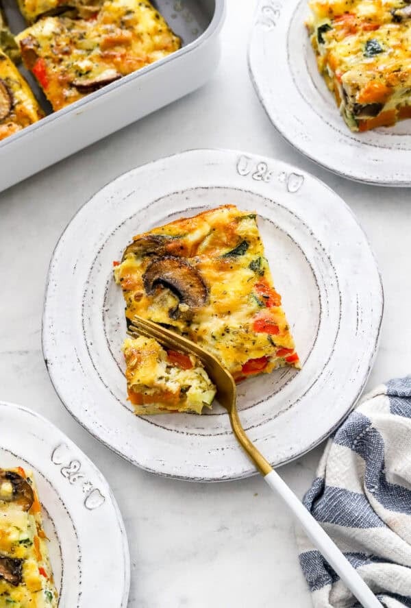Cut slice of frittata on a plate with a fork with more plates of it around it.