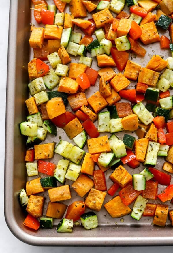 Roasted veggies on a baking sheet with seasoning on them.
