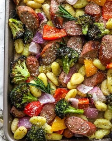 Sheet pan gnocchi and sausage with veggies with herbs on it.