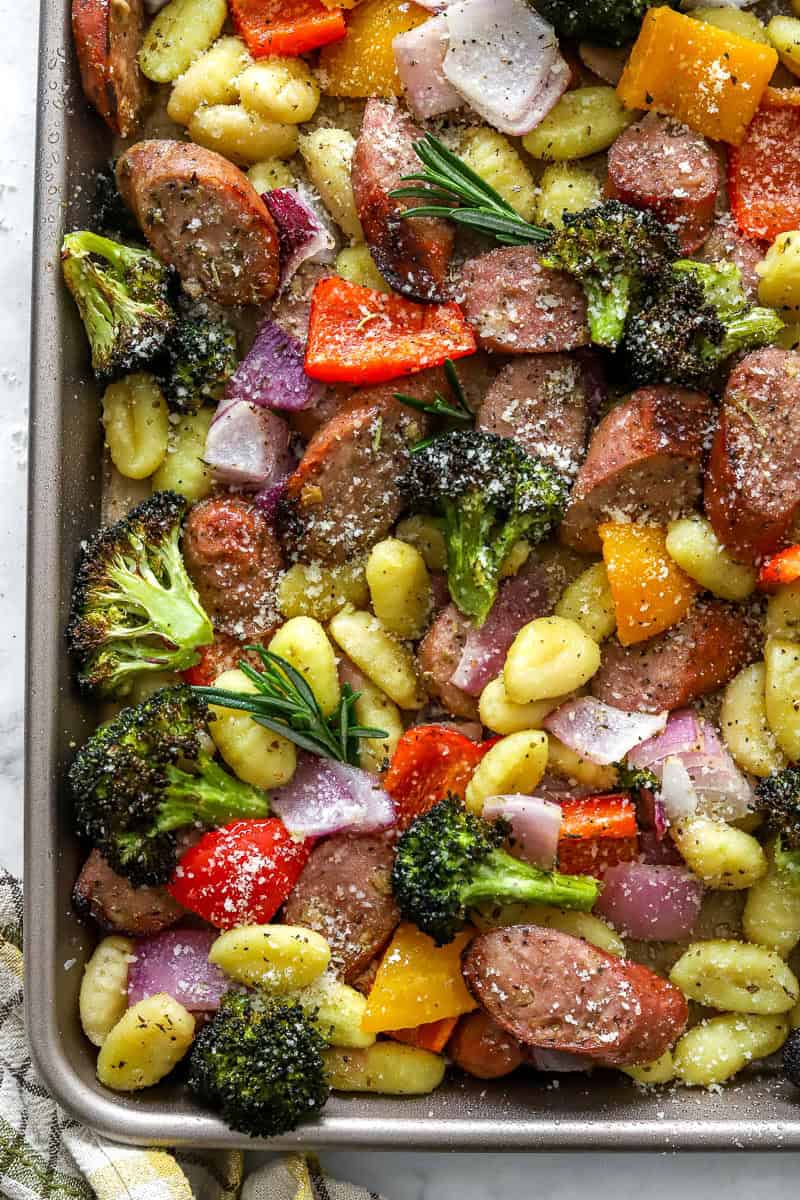 Sheet pan gnocchi and sausage with veggies with herbs on it.
