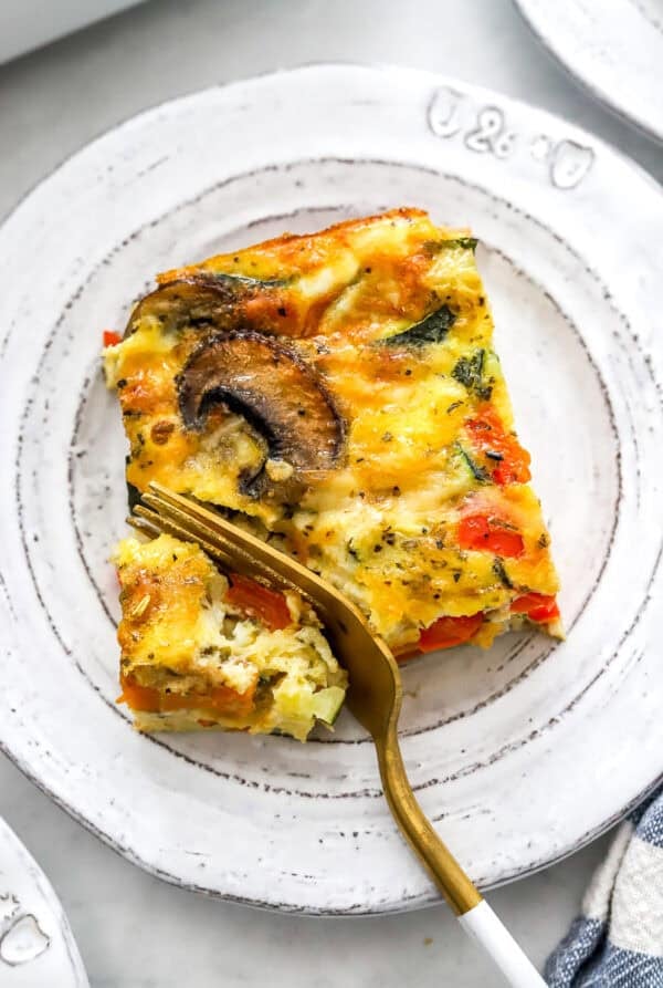 Square slice of baked vegetable frittata on a plate with a fork cutting into it.