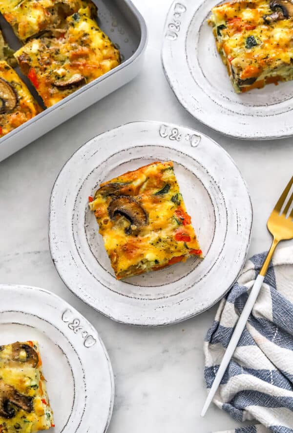 Cut pieces of veggie egg baked frittata on plates with more behind it.