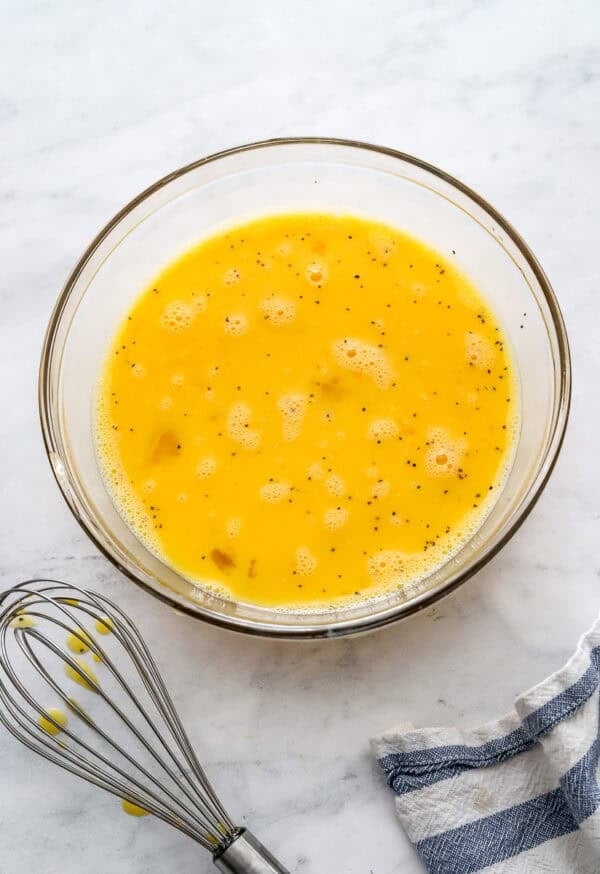 Whisked eggs in a glass bowl with a metal whisk in front of it.
